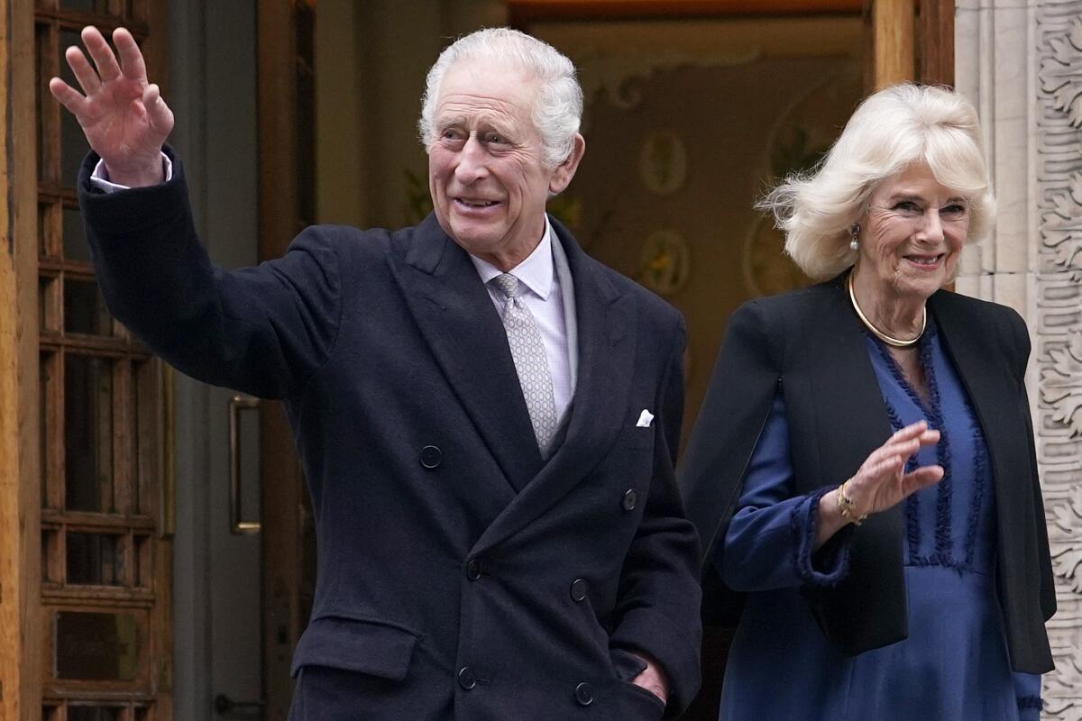 Britain's King Charles III and Queen Camilla wave outside a building.