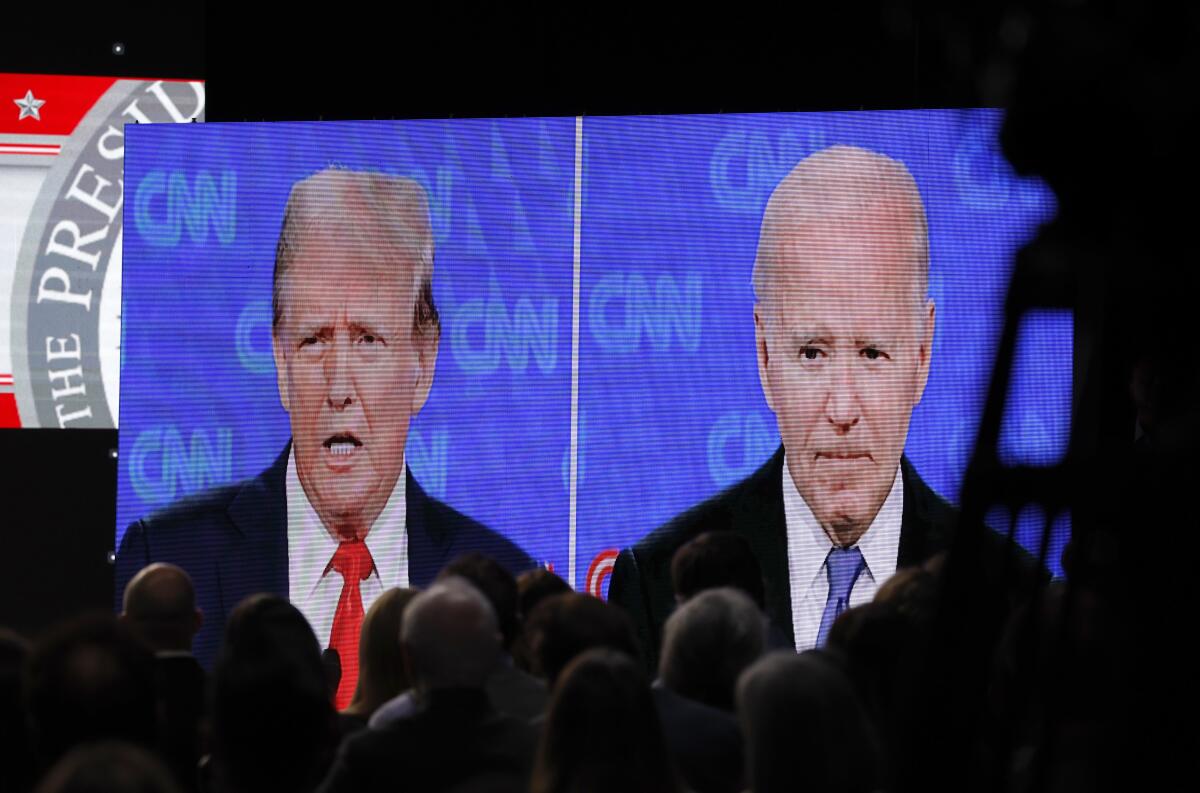 Debate watchers are silhouetted against a large video screen showing Biden and Trump.