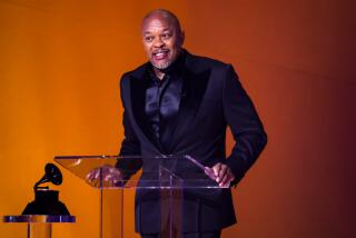Dr. Dre in a suit speaking onstage at a lectern