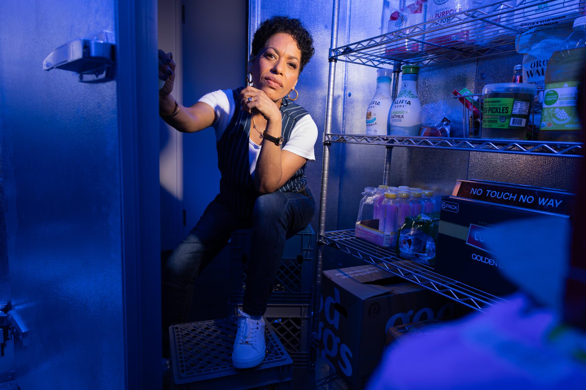 A person crouches in a restaurant supply room lit with blue light