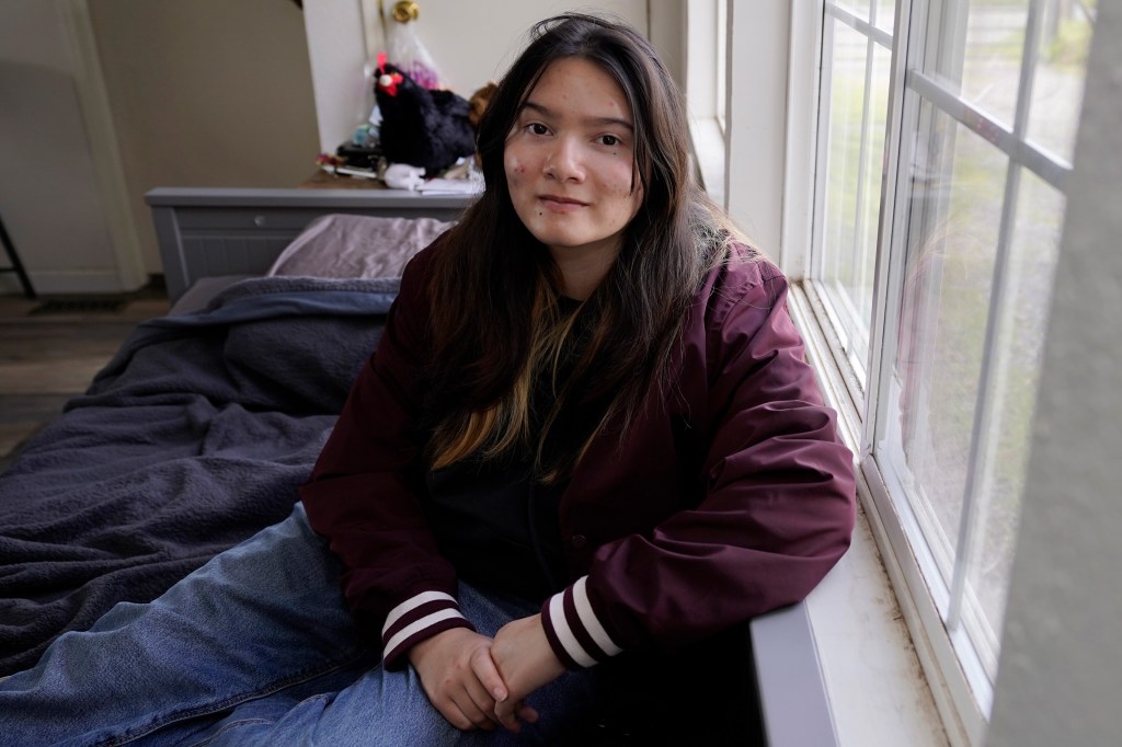 A photo of a teenager posing for a portrait by a window indoors.