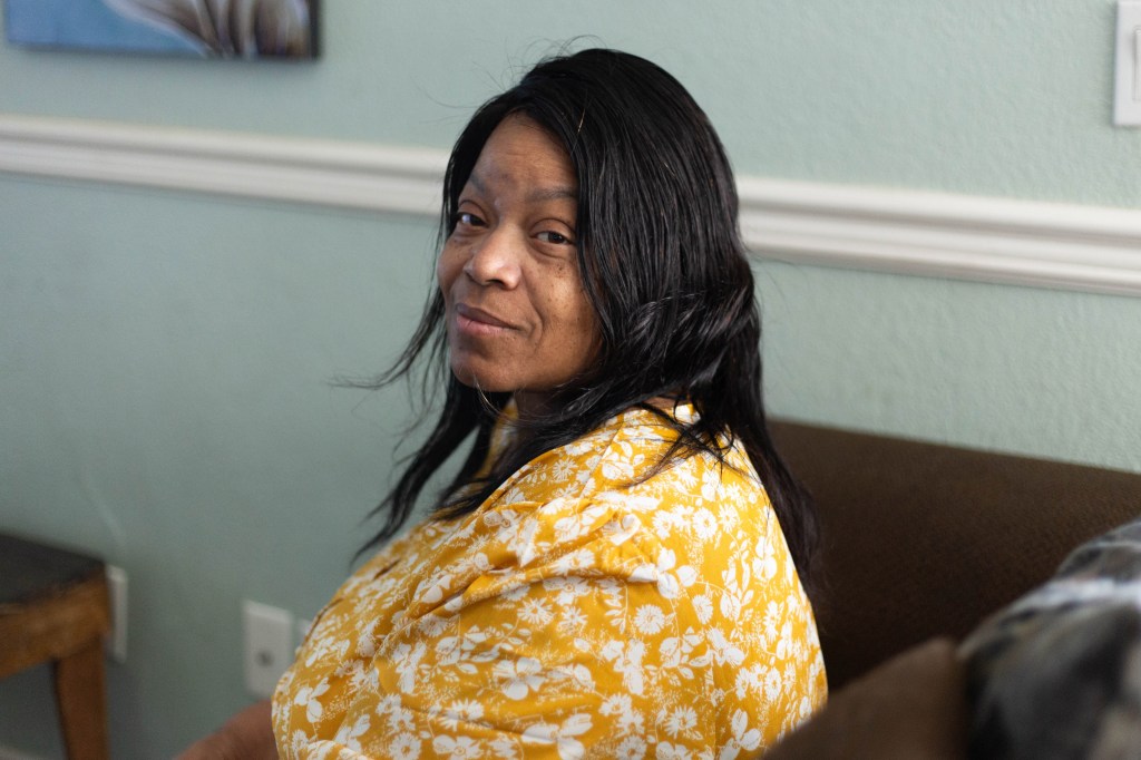 Teresa Johnson is sitting on a couch in her home. She is turning her head to look towards the photographer.