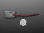 Overhead shot of sewable DC jack connector with black and red wires above a US quarter for scale.