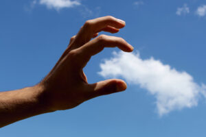 A hand acting as if it can grasp a cloud in the sky, shot from an angle to make it look real.