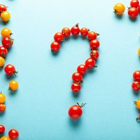 Red and yellow cherry tomatoes, some forming a question mark, against a light blue background. (organic, fruits, vegetables)