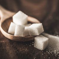 Zoomed in photo of a pile of sugar cubes in a wooden stop on a wooden table.