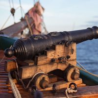 Old medieval wooden pirate military war ship with a cannon on the deck pointed out and aiming