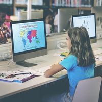 Grade school students working at computers in a school library. Study learn girl child class technology