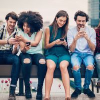 Multi-ethnic group of people sitting on an urban bridge text messaging and sharing smart phone content.