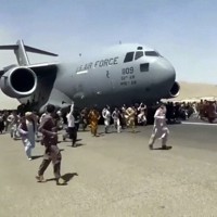 アフガニスタンの首都カブールの国際空港で、米軍機のそばを走る人々＝カブールで16日、AP