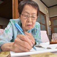 家族写真を手元に置いて体験を書き記す堀田昭子さん＝広島市安佐北区で2023年8月1日、根本佳奈撮影