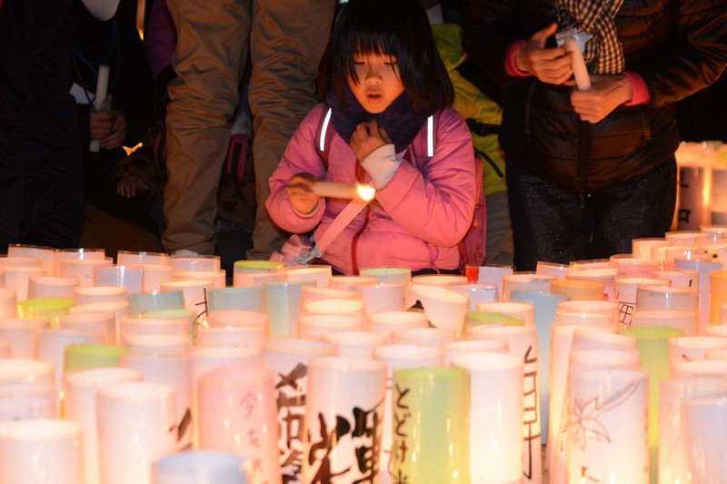 会場に並んだ灯籠にろうそくで火をつける来場者＝神戸市中央区の東遊園地で2024年1月16日午後5時48分、山本康介撮影