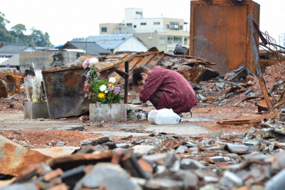 輪島朝市の火災現場で花を手向け、30秒ほどにわたって手を合わせた女性。世話になった知人が亡くなったという＝石川県輪島市で2024年5月1日午後4時10分、阿部弘賢撮影