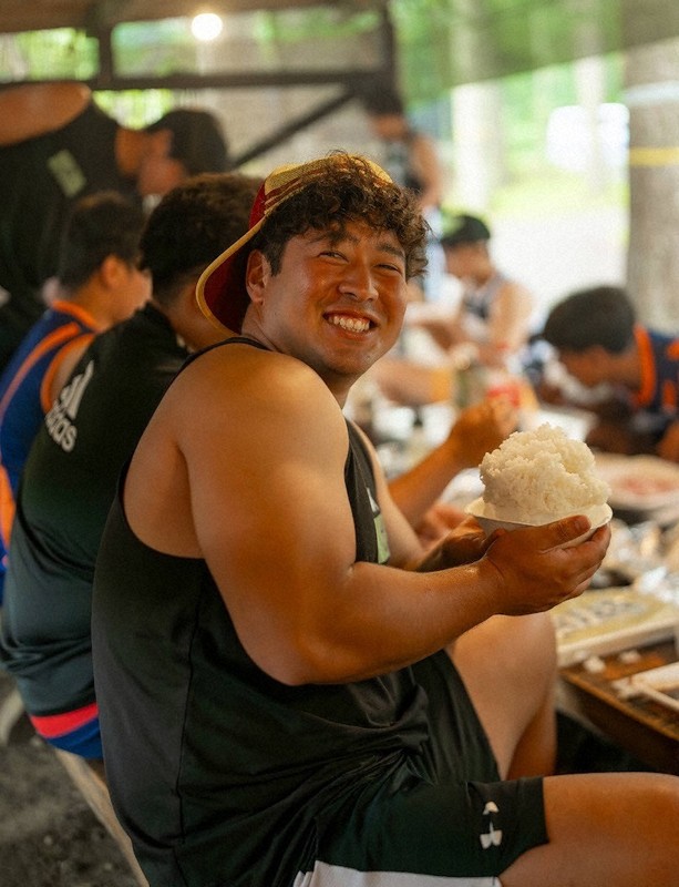 菅平合宿中のバーベキュー大会で大盛りの白飯を手に笑顔を見せる、拓大の村松俊介選手（4年）＝拓大ラグビー部提供　©渡辺周治