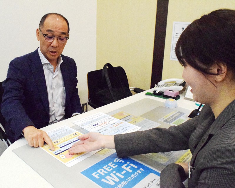 きらぼし銀行・烏山支店の藤山未紗さん（右）から定期預金の金利などの説明を聞く男性＝東京都世田谷区で2024年11月25日、竹地広憲撮影