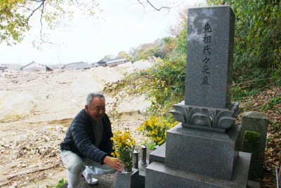 集落で唯一残ったという南家の墓を手入れする南仁さん。土砂の向こうに崩れた自宅の屋根が見えた＝石川県珠洲市仁江町で2024年11月25日、稲生陽撮影