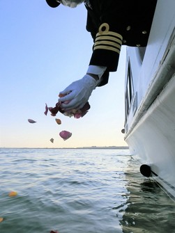 This image provided by House Boat Club Co. shows flower petals being scattered at sea by a staffer after the dispersal of a person's remains.