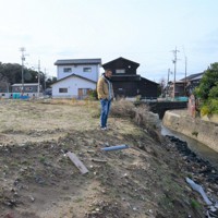 自宅があった場所に立つ北浜正義さん。能登半島地震の影響で裏手の川の護岸が崩れ、自宅は後方に傾いた後、裂けるように損壊した＝石川県珠洲市蛸島町で2024年12月20日午後0時26分、阿部弘賢撮影