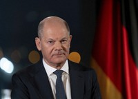 German Chancellor Olaf Scholz sits in front of the backdrop of the Reichstag illuminated by spotlights during a photo session after the recording of his New Year's address in the Chancellery in Berlin, Germany, Dec. 29, 2024. (Soeren Stache/dpa via AP)