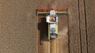 A top-down aerial view of a combine harvester moving across a field of grain, to represent supply chain emissions in the food industry.