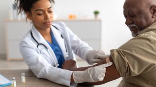 A doctor places a bandaid on a man's arm after giving him a vaccine