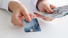 A woman's hand holds a cash back credit card and U.S. hundred dollar bills.