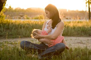 A woman breast-feeds her baby outdoors.