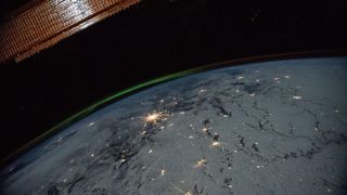 a photograph of a green aurora with sparkling city lights taken from the International Space Station