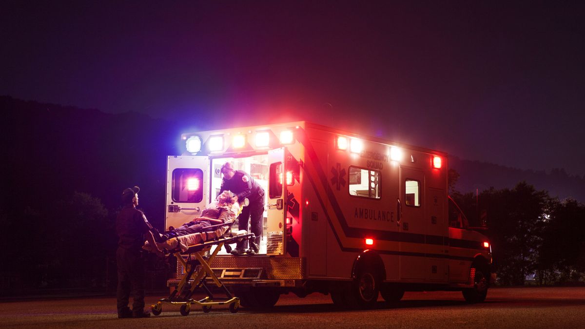 An ambulance parked at night in the US, with two paramedics wheeling a patient in.