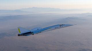 a needle-nosed white and silver plane flies over a desert-mountain landscape