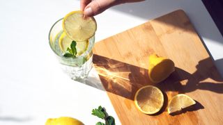 Lemon slices on a chopping board with a person putting several slices in a glass of water