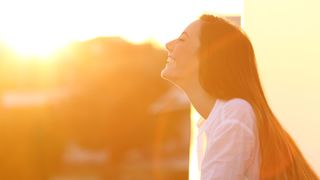 Side view portrait of a happy woman breathing deep fresh air at sunset in a house balcony