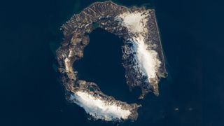 A satellite photo of a horseshoe-shape island partly covered in snow