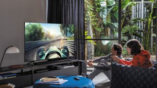 The Samsung Q70T QLED in a living room while a family watch it and play a video game on it.