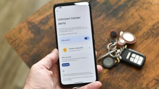 Unknown tracker alerts screen on an Asus phone with keychain and AirTag behind