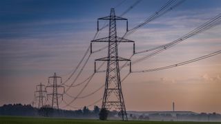 Electricity pylons pictured at dusk in an empty field.