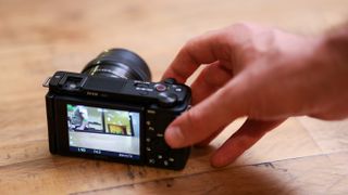 A hand operating the Sony ZV-E10 while it sits on a wooden table