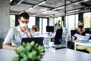 Man wearing medical mask uses laptop in the office