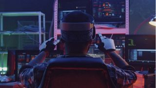 Rear facing image of man sat in dark tech lab using VR headset and gloves 