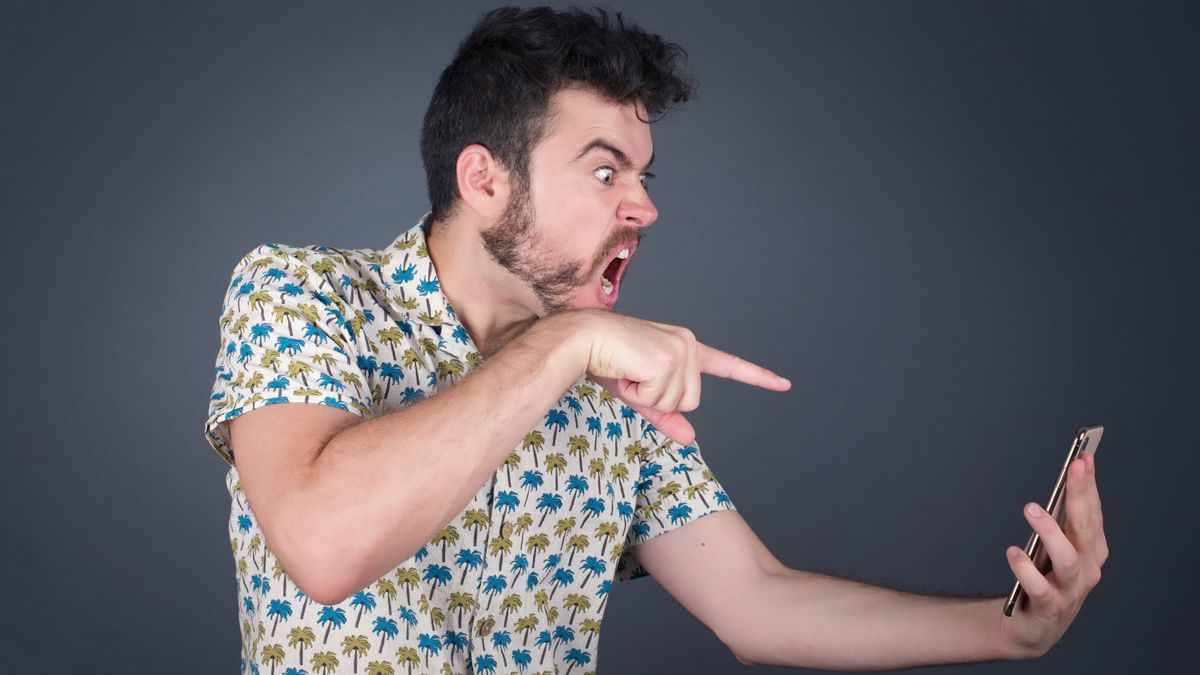 A man shouting and pointing angrily at the smartphone in his hand.