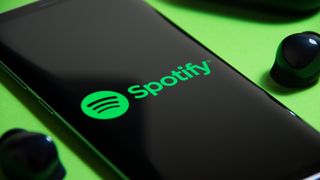 Die Spotify-App auf einem Smartphone, daneben liegen ein Paar kabelloser Ohrstöpsel