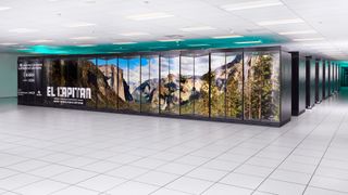 A photo of the El Capitan Supercomputer housed in its secure facility at Lawrence Livermore National Laboratory (LLNL). It looks like cabinets with a photo of El Capitan at Yosemite National Park, with blue-green LEDs lighting the white ceiling above it and white tiled floors in front of it.