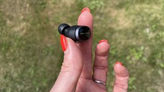 Bowers & Wilkins Pi8 earbuds, held in a hand on grassy background