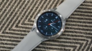 En grå Samsung Galaxy Watch 4 Classic ligger med urtavlan vänd uppåt på en mönstrad duk.