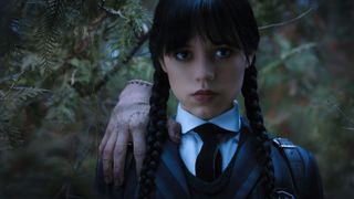 Lähikuvassa Wednesday Addams ja Thing vihreää puustoa vasten