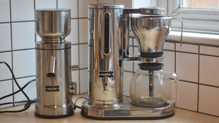 Image of the Aarke Coffee System – a stainless steel coffee bean grinder and drip coffee maker – positioned on a kitchen counter