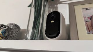 Arlo Essential 2K står i en hylla mellan en vas och en fotoram.