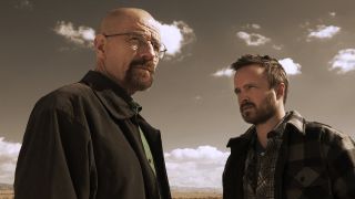 Walter White looking off into the distance while Jesse Pinkman looks at him with the sky behind them.