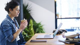 Student holding a cup of coffee and using a YouTube download app to watch a video at her desk