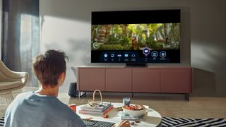 The Samsung Neo QLED TV in a living room on a TV stand while someone watches it.